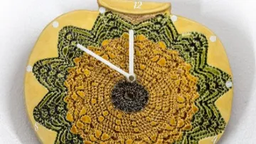 Uhr in Sonnenblumenform mit Häkelmuster und Zeigern.