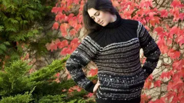 Person wears knitted sweater near red leaves.