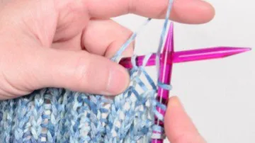 Handstricken mit rosa Nadeln und blauem Garn.