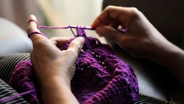 Hands crocheting with purple yarn indoors.