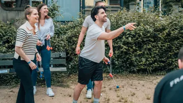 People playing an outdoor tossing game, smiling.