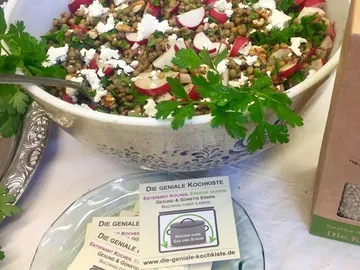 Schüssel mit Linsensalat und frischen Kräutern auf Tisch.