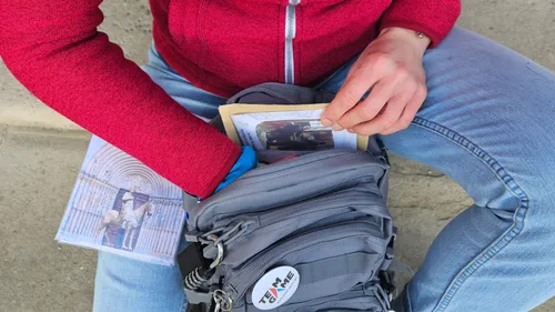 Die Person holt Fotos aus einem grauen Rucksack im Freien ab.