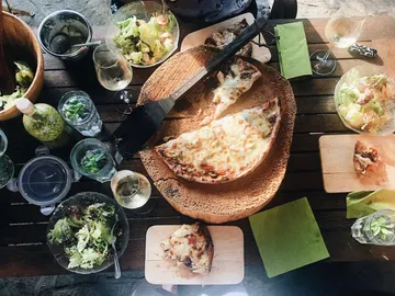 Pizza is on a wooden board surrounded by salads and drinks.