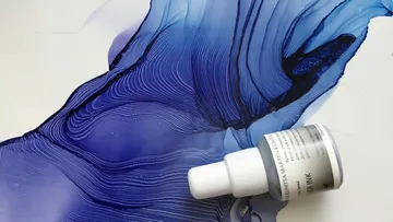 Eine Flasche Tinte auf abstrakter blauer Malerei.
