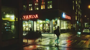 Person am Zebrastreifen in der Nähe eines beleuchteten Cafés in der Nacht.