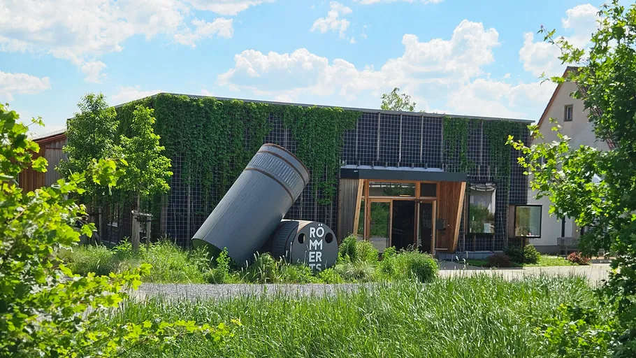 Large beer can sculpture in tall grass, outside a building.