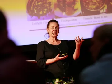 Woman talking, holding a phone, in front of a screen.