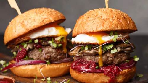Two gourmet burgers with egg yolk and greens.