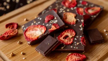 Dunkle Schokolade mit getrockneten Erdbeeren auf einem Holzbrett.