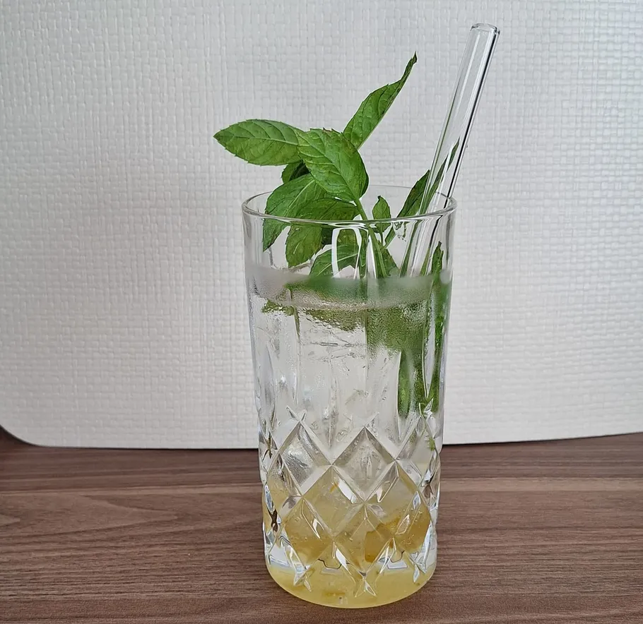 Glass with mint leaves and straw indoors.