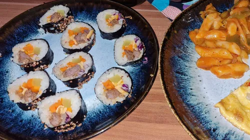 Teller mit Kimbap und würzigen Reiskuchen.