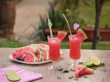 Two pink cocktails are on the table next to watermelons.