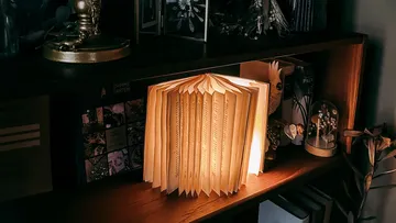 A glowing book-shaped lamp on a wooden shelf.