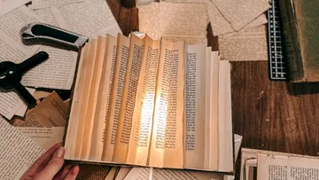 Person, die ein beleuchtetes Buch auf einem überfüllten Tisch hält.