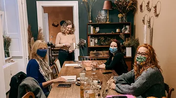 Vier maskierte Frauen sitzen an einem Tisch.