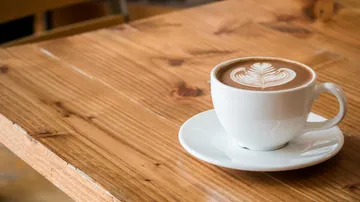 Latte with art in white cup on wooden table.