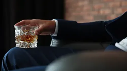 Person holding whiskey glass in relaxed setting.