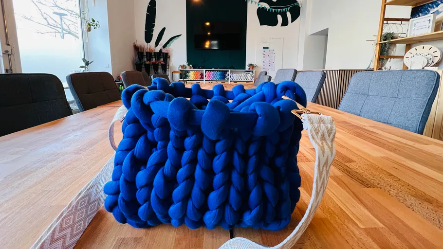 Blaue gestrickte Tragetasche auf einem Holztisch.