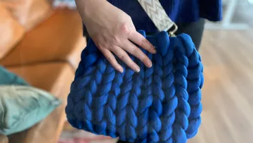 Hand holding a blue woven bag indoors.