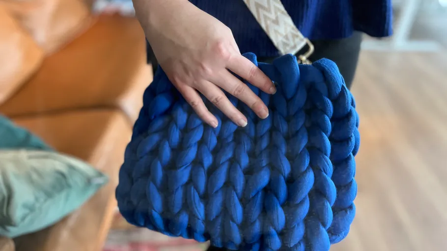 Hand, die drinnen eine blaue gewebte Tasche hält.