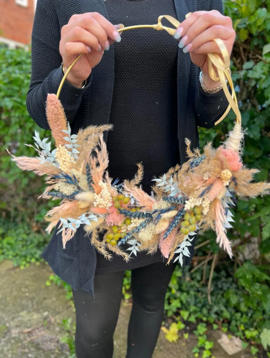 Person holding decorative floral wreath outdoors.