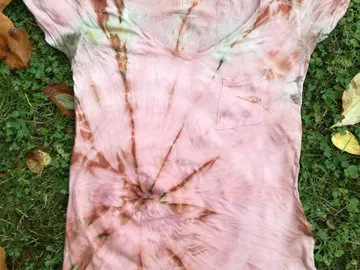 Pink t-shirt lying on green grass with a leaf-decorated background.