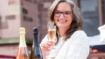 Frau mit Champagnerglas draußen, lächelnd.