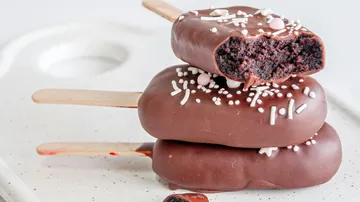 Drei Schokoladen-Cake-Pops mit Streuseln auf Stäbchen.