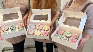 Drei Personen halten Schachteln mit dekorierten Cupcakes in der Hand.