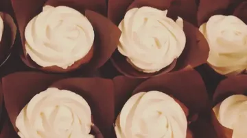 Cupcakes mit weißem Zuckerguss in braunen Verpackungen.