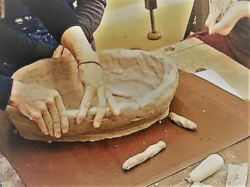 Hands form clay into a bowl on a table.