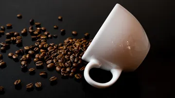 Coffee beans spilling from tipped cup.