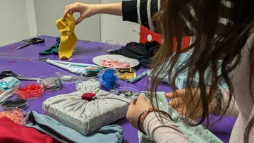 Zwei Personen, die Geschenke mit Stoff auf dem Tisch verpacken.