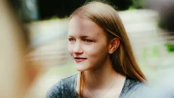 Young woman smiling outdoors, blurred background.