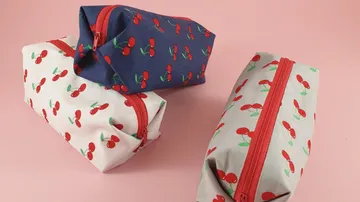 Three cherry-patterned zipper pouches on pink background.