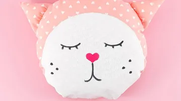 Cat-face pillow with pink ears and hearts.