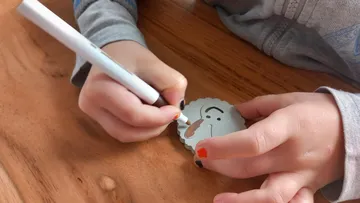 Kind zeichnet auf einer kleinen Gesichtsscheibe mit Marker.