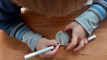 Child coloring a small paper face at table.