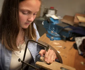 Young girl using saw in workshop.