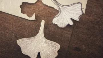 Metal leaf cutouts and paper outline, wooden surface.