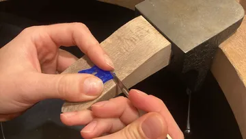 Hands carving blue wax on a wood bench.