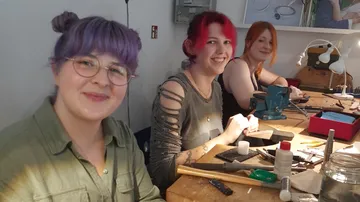 Three people sitting at workbench crafting.