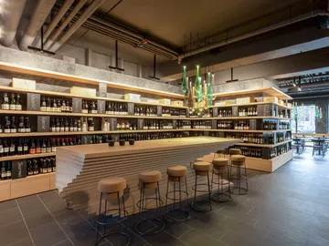 Modern bar with shelves full of drinks, wooden counter and chairs.