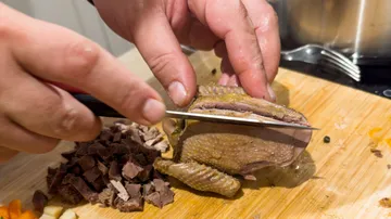 Hands slicing roasted pigeon on cutting board.