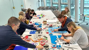 Personen gestalten Kunst mit Bändern auf Tisch.