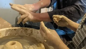 Hände formen Ton auf einer Töpferscheibe.