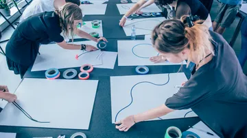 People creating art with tape on tables.