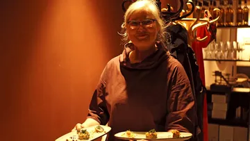 Frau lächelnd, hält Teller mit Essen drinnen.