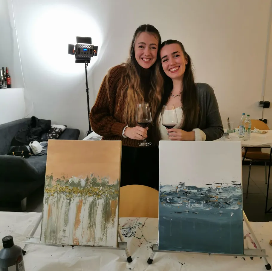 Two women smiling with paintings and wine.